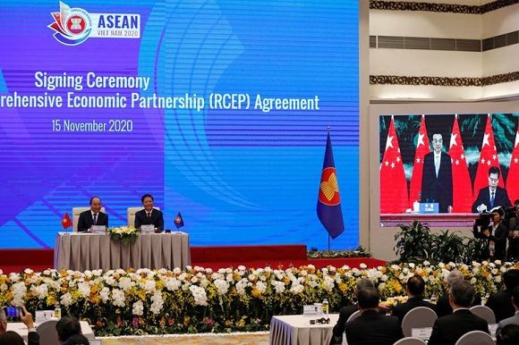 El primer ministro de Vietnam', Nguyen Xuan Phuc (I) junto al ministro de Industria y Comercio Tran Tuan Anh viendo por una pantalla al ministro de Comercio de China Zhong Shan (D) y al primer ministro Li Keqiang firmando el documento de fundación del RCEP durante una cumbre en Hanoi. Nov 15, 2020. Foto: Reuters.